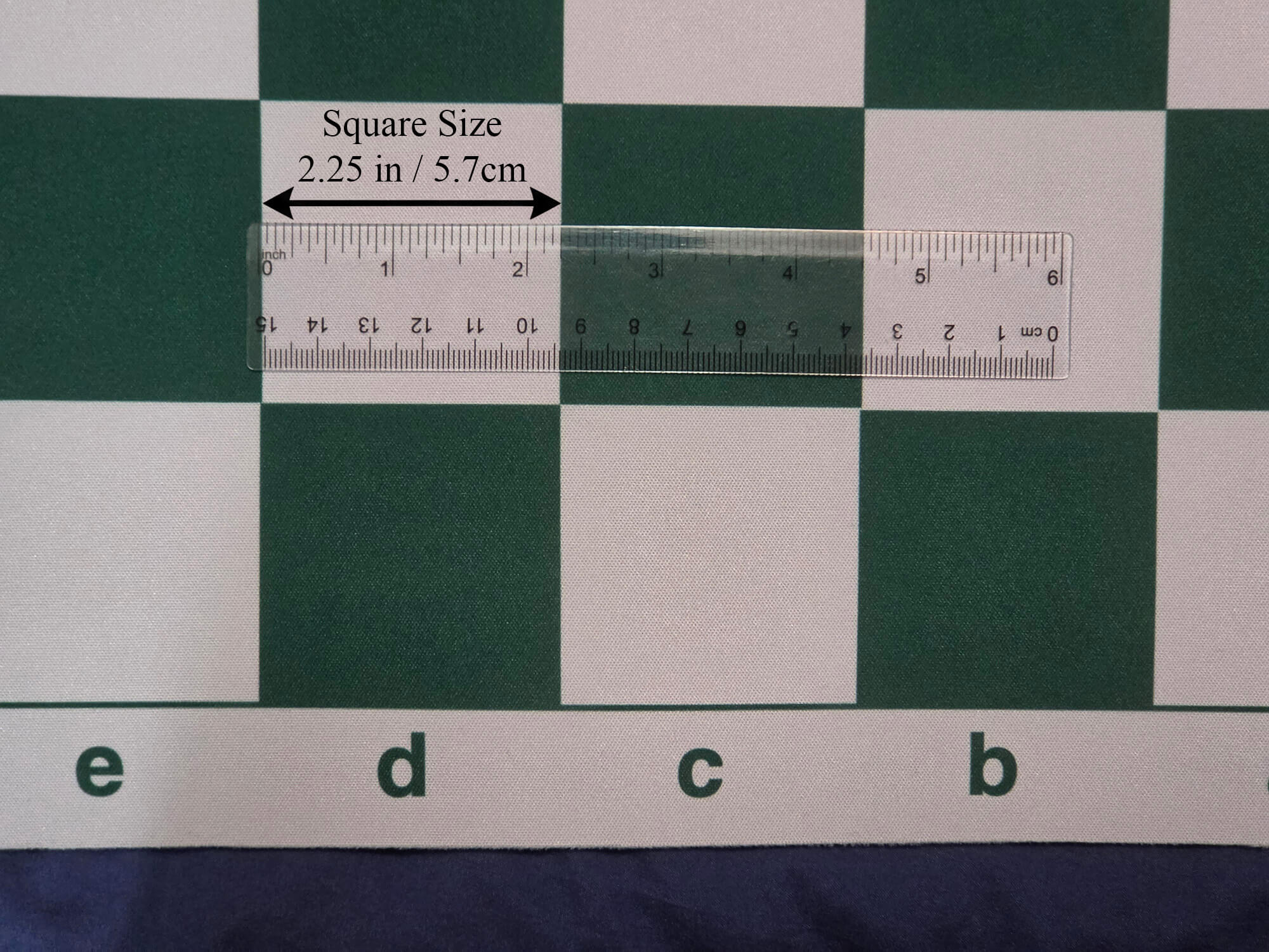 High-definition close-up product photograph of a green and white mousepad chess board section with a transparent ruler and callout labels verifying the 2.25-inch square dimension.
