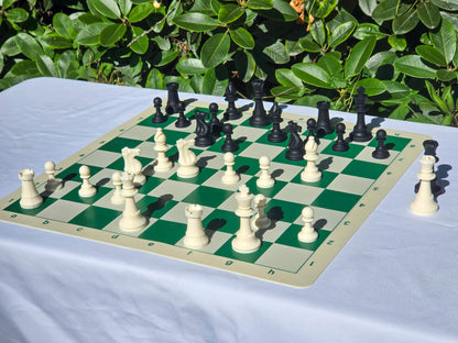Angled view of black and white silicone chess pieces on the green side of a double-sided board outdoors.