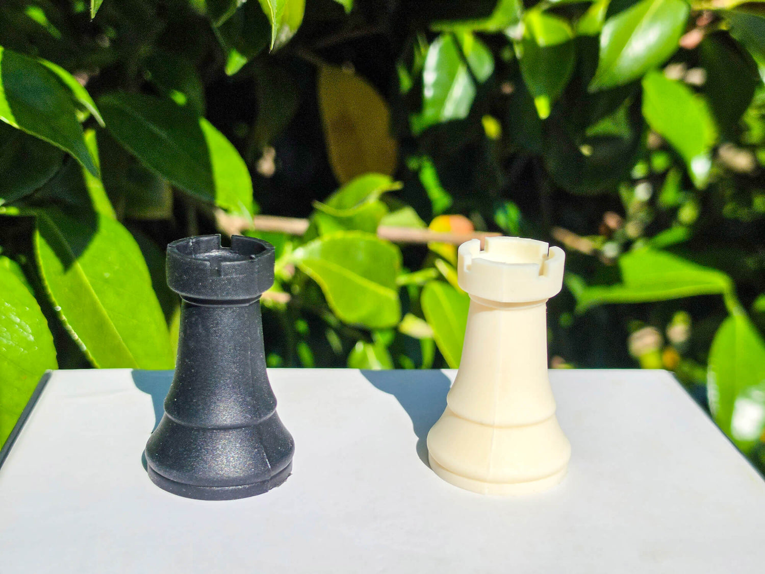 Close-up of black and white silicone chess rook pieces with green foliage behind them.