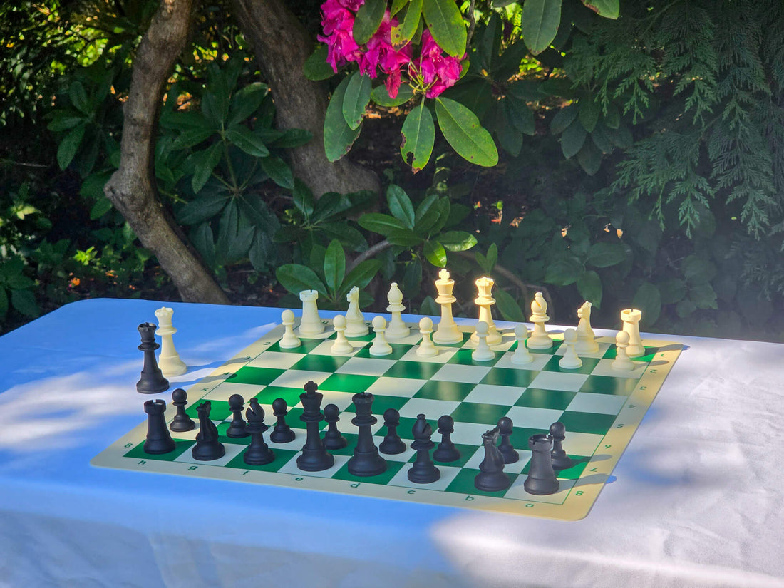 Full silicone chess set with black and white Staunton pieces arranged on the green side of the double-sided board outdoors.