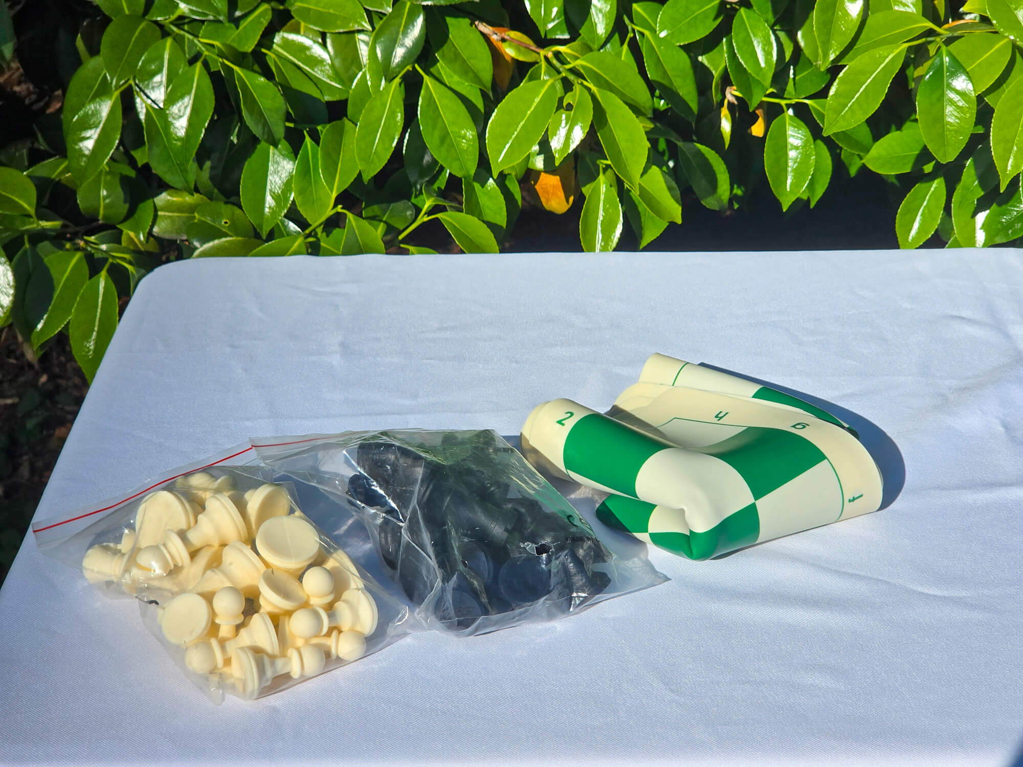 Unpackaged silicone chess set showing loose black and white pieces alongside a folded double-sided silicone board.