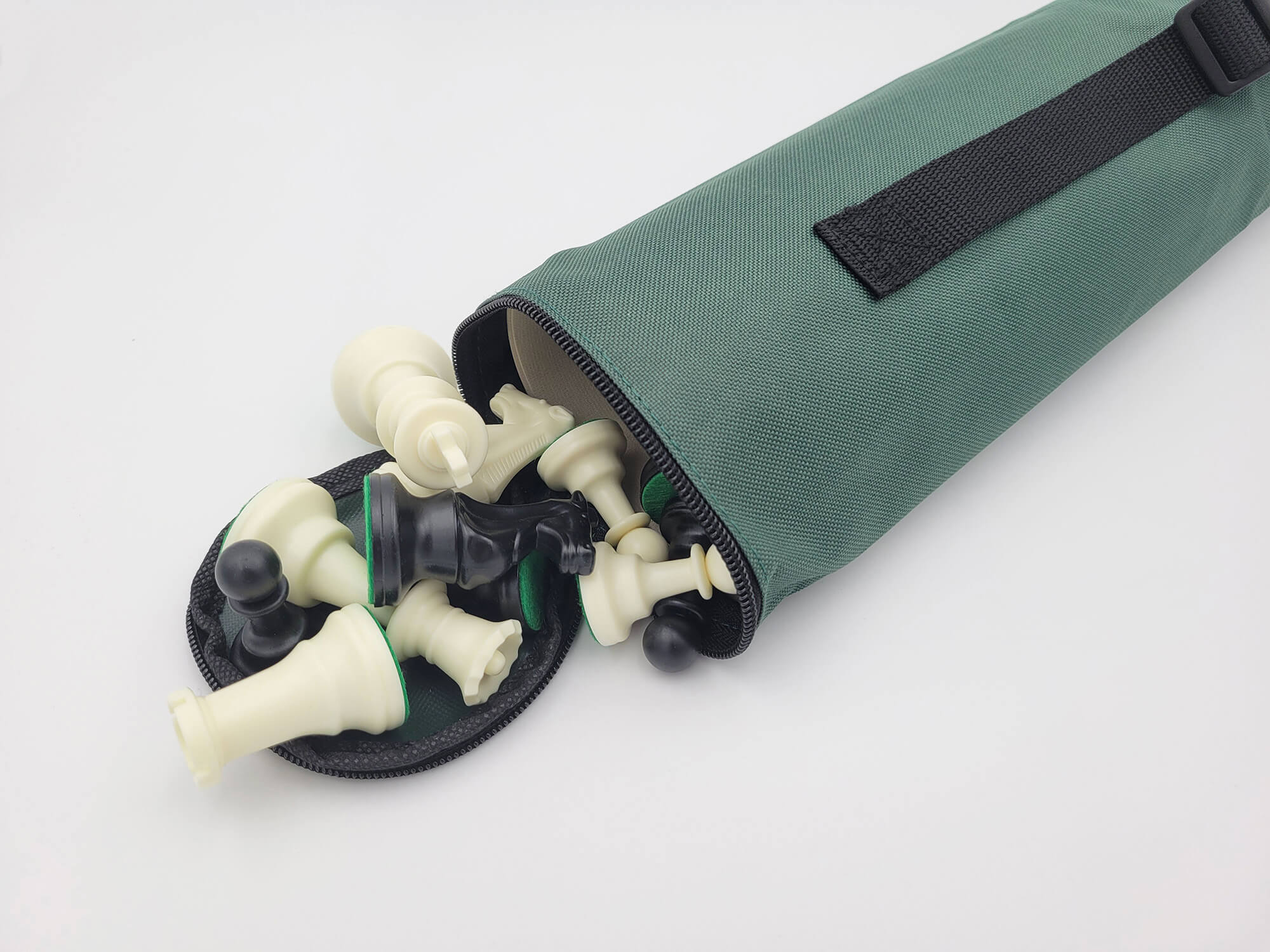 Close-up of black and white plastic Staunton chess pieces spilling out of a forest green canvas quiver carrying bag with a black shoulder strap.