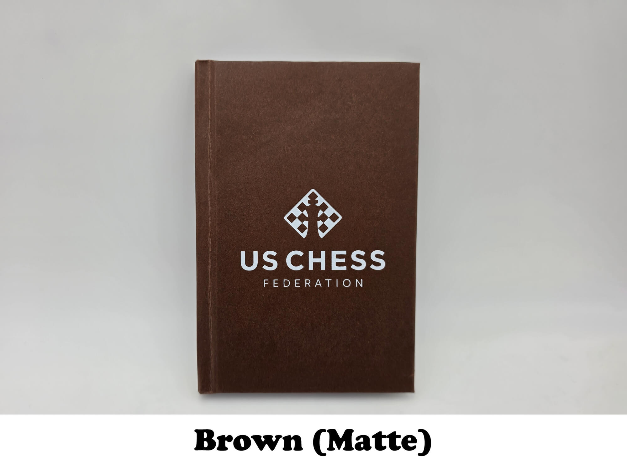 Matte finish brown USCF chess notation scorebook with official logo.