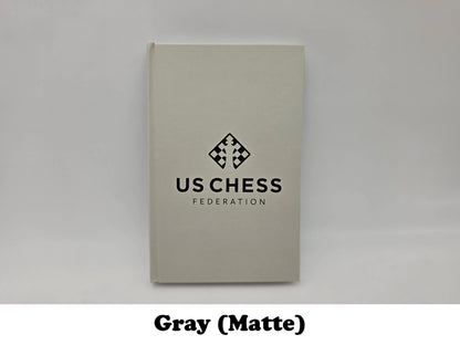 Matte light gray USCF official chess scorebook.