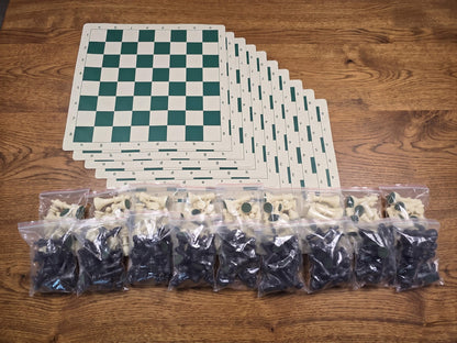 A wholesale lot of 10 standard tournament-size Staunton chess sets displayed on a wooden table, featuring 10 stacked rollup green and white chess boards and 10 pairs of resealable bags containing a full set of black and white plastic chess pieces.